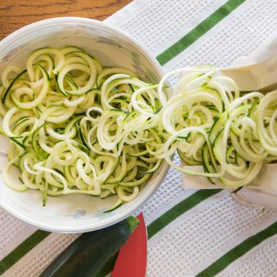 Spiralized zucchini noodles in a bowl with spializer tool.