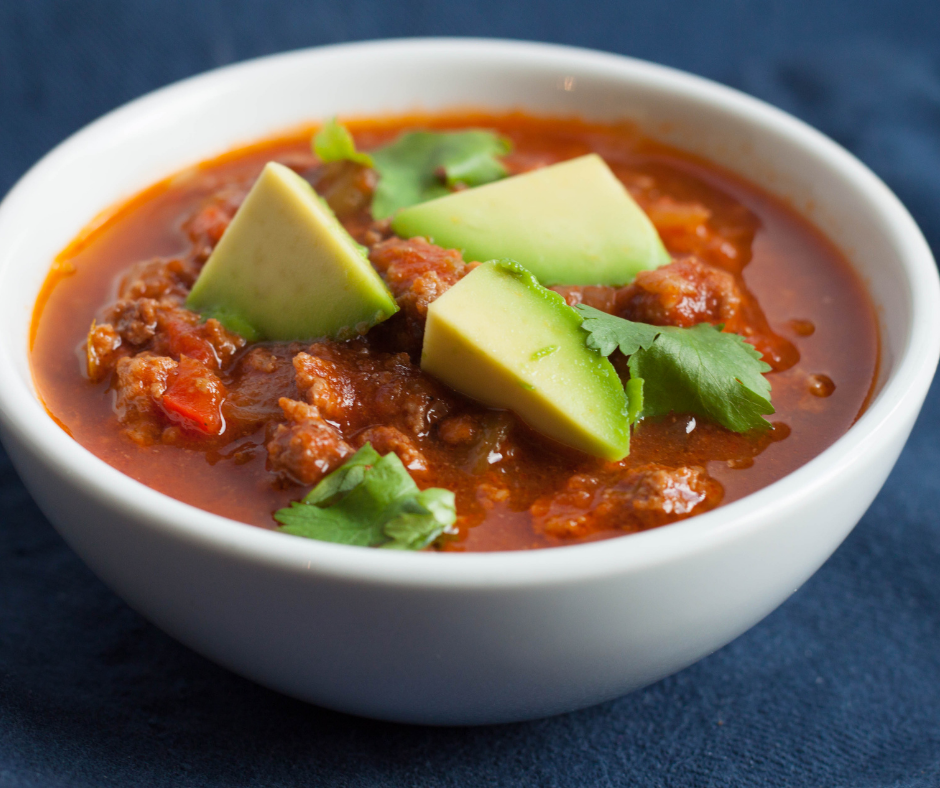  A bowl of healthy grass-fed beef chili with avocado and cilantro as a topping.