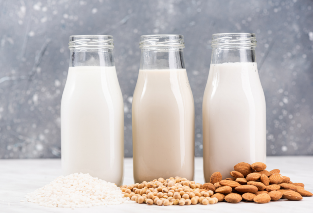 Bottles of different types of milk on a table surrounded by different types of nuts.