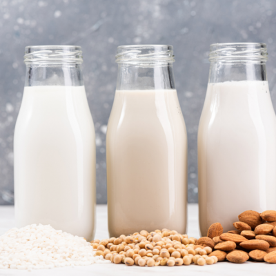 Bottles of different types of milk on a table surrounded by nuts and powder.
