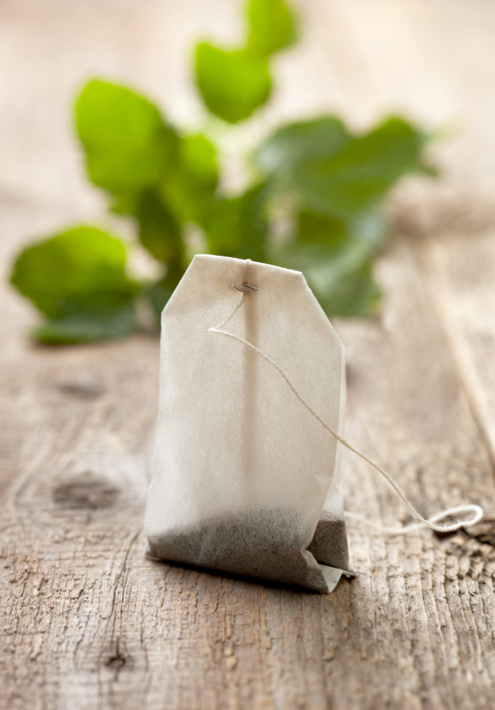 Tea bag sitting on table with leaves in the background.
