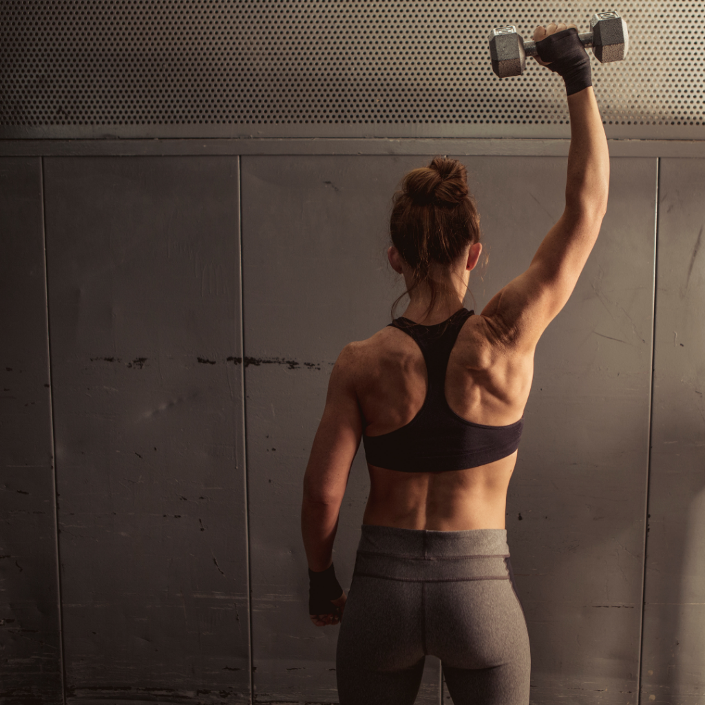 Fit woman holding a dumbbell over her head.