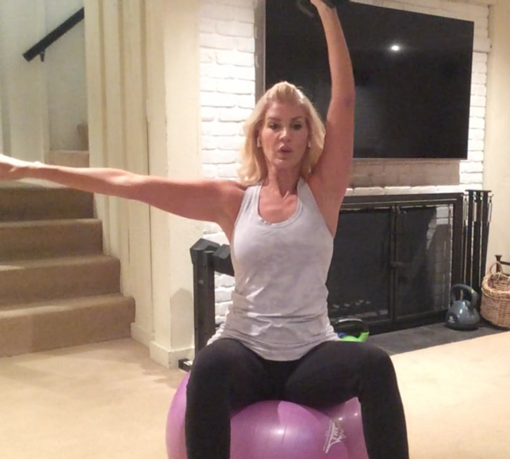 Pretty woman sitting on a stability ball performing a one arm shoulder press with a dumbbell.