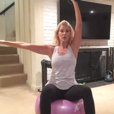Pretty woman sitting on a stability ball performing a one arm shoulder press with a dumbbell.