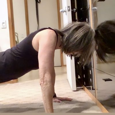Fit older woman performing a hand plank on the floor.