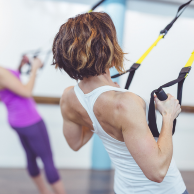 Woman using a TRX suspension trainer in a class. Shows her toned back.