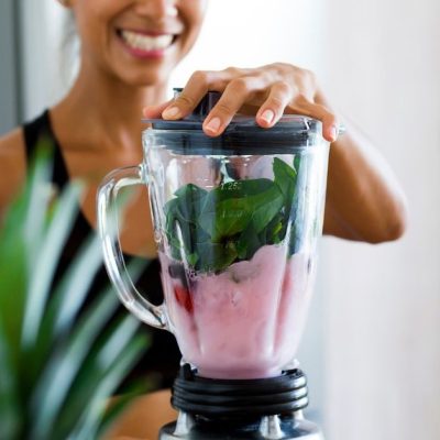 Healthy woman making a shake with greens and berries.