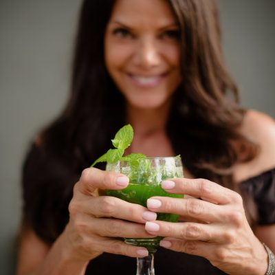 Woman holding a healthy green smoothie cheering and smiling.