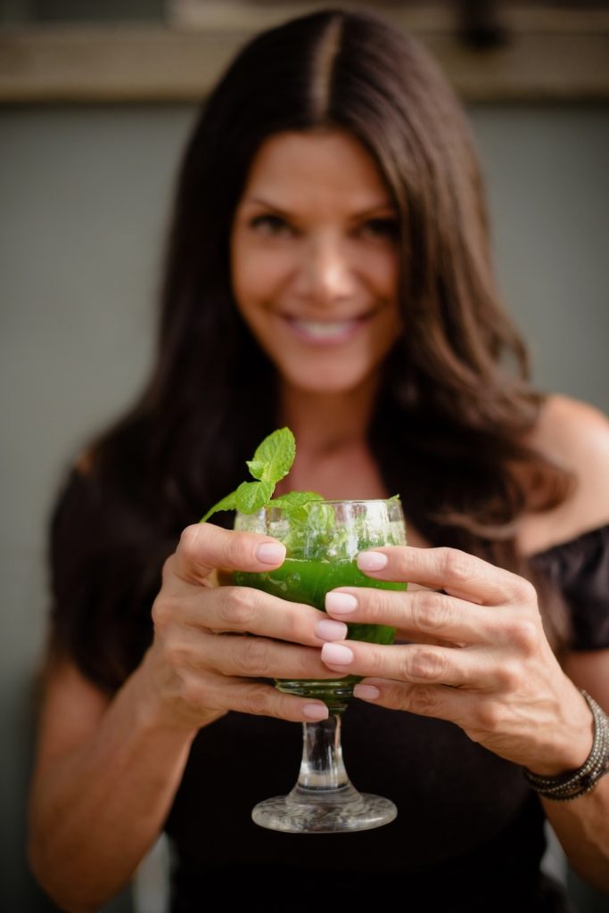 Woman holding a healthy green smoothie cheering and smiling.
